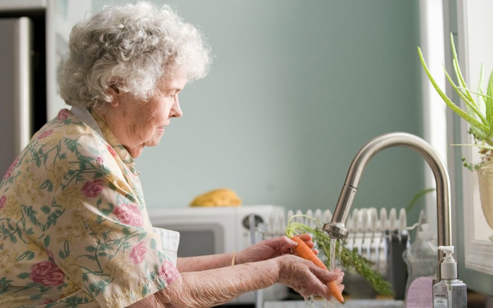 An older woman washing carrots at her kitchen sink