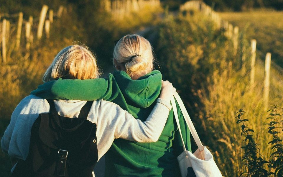Two people walking through tall grass, one with an arm around the other